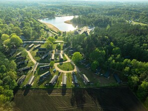 Vista aérea de un camping con varias cabañas, una zona de encuentro central y un lago.