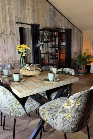 Un comedor con mesa de madera, sillas tapizadas con motivos florales y un jarrón decorativo con girasoles.