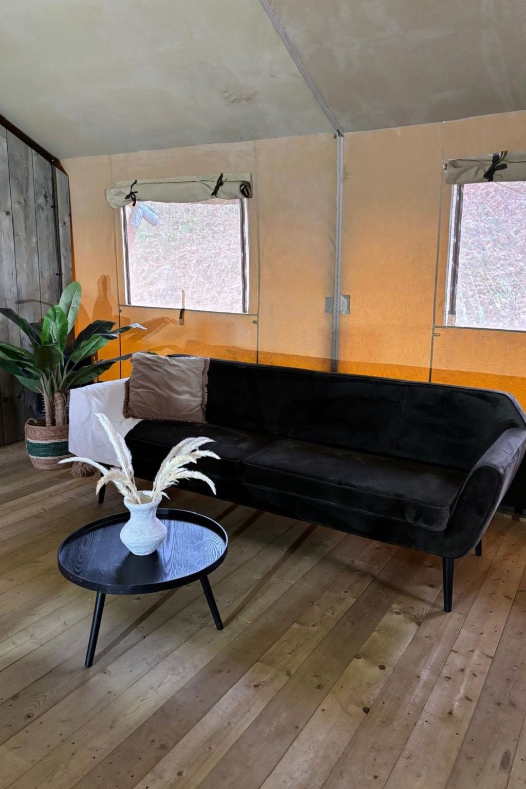 Ein Zimmer mit einem schwarzen Sofa, einem runden Tisch mit einer Vase und einer Topfpflanze.