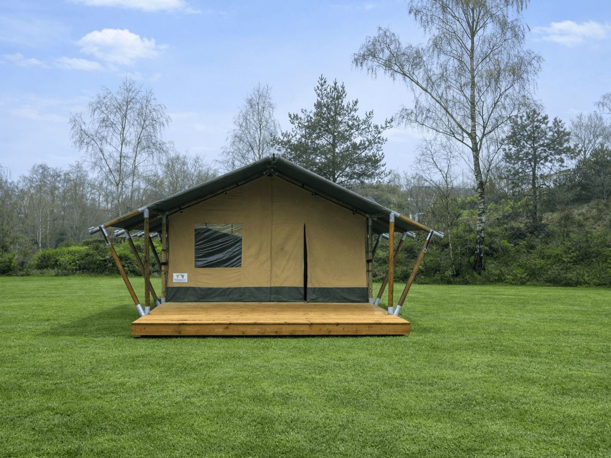 Een eenpersoonstent met houten platform, een raam en een deur, gelegen op een grasveld met bomen op de achtergrond.