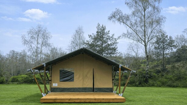 A single-room tent with a wooden platform, a window, and a door, set on a grassy field with trees in the background. - Wilsumer Berge Resort - Glamfield Lodge 2p by Interhome (Wilsum)