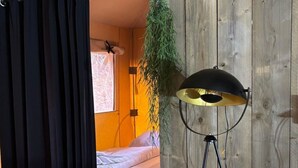 A room with a bed, a hanging plant, a floor lamp, and a curtain. - Wilsumer Berge Resort - Glamfield Lodge 2p by Interhome (Wilsum)