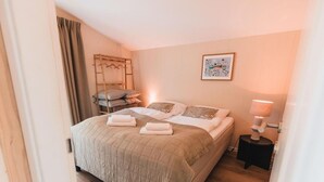 Ein ordentlich bezogenes Bett mit Kissen und Decke, ein Nachttisch mit Lampe und eine Holzleiter an der Wand.