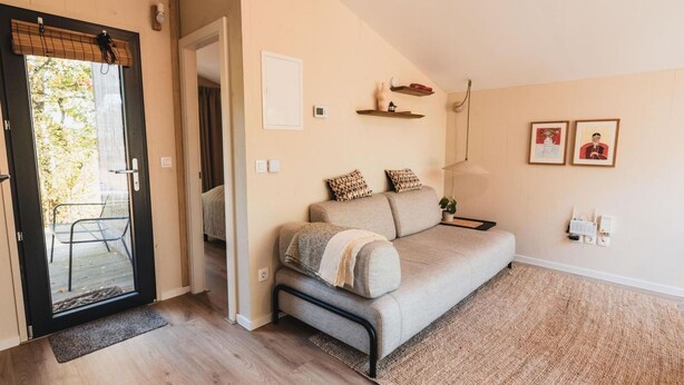 Ein gemütliches Wohnzimmer mit einer Couch, einem kleinen Tisch und einer Tür, die zu einem Außenbereich führt.