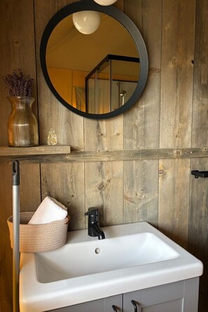 A bathroom with a white sink, a round mirror with a black frame, and a wooden wall. - Wilsumer Berge Resort - Glamfield Lodge 4p by Interhome (Wilsum)