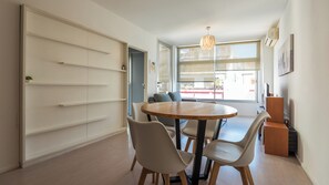 Et spiseområde med et rundt bord og stole, en sofa og et stort vindue med udsigt.