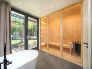Un bagno moderno con una vasca freestanding, una sauna in legno e un'ampia porta scorrevole in vetro che dà su un patio.