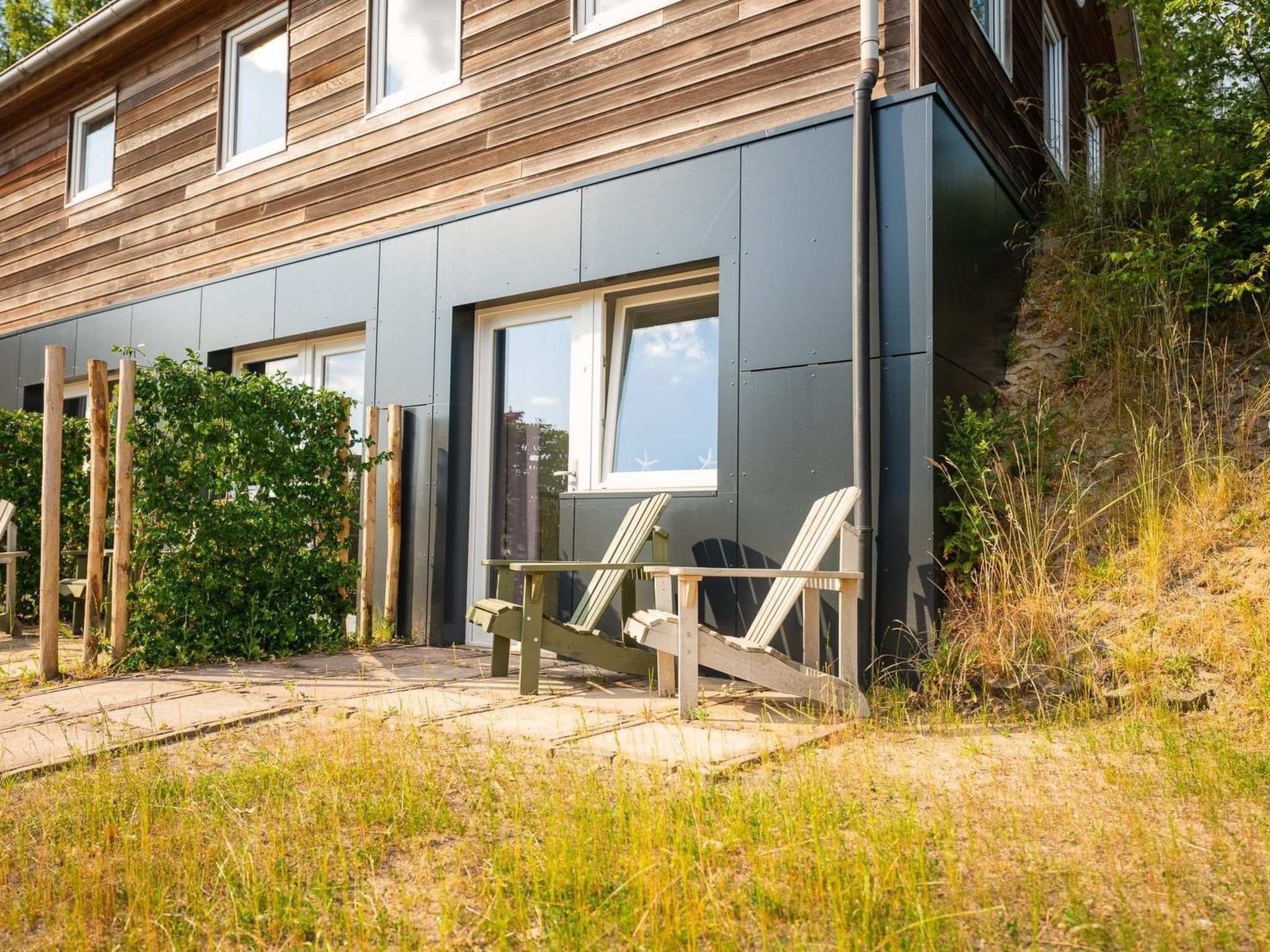 A modern house with a grey exterior, large windows, and a wooden deck with chairs.