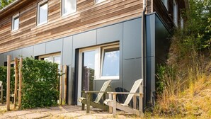 A modern house with a grey exterior, wooden deck, and a small garden area. - Wilsumer Berge Resort - Trekkershut by Interhome (Wilsum)