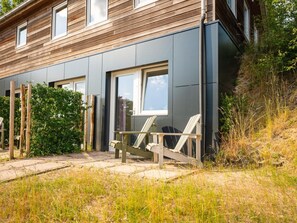 A modern house with a grey exterior, large windows, and a wooden deck with chairs.