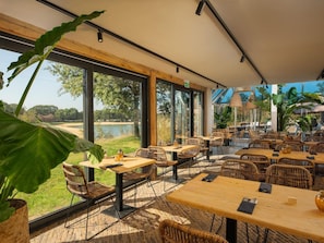 Un'area pranzo all'aperto con mobili in vimini, ampie finestre e vista su un lago.