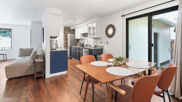 Eine moderne Küche mit weißen Schränken, einer zentralen Kochinsel und einem Essbereich mit einem Holztisch und Stühlen.