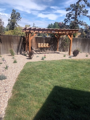 A wooden pergola structure in a backyard with a gravel pathway and a grassy lawn.
