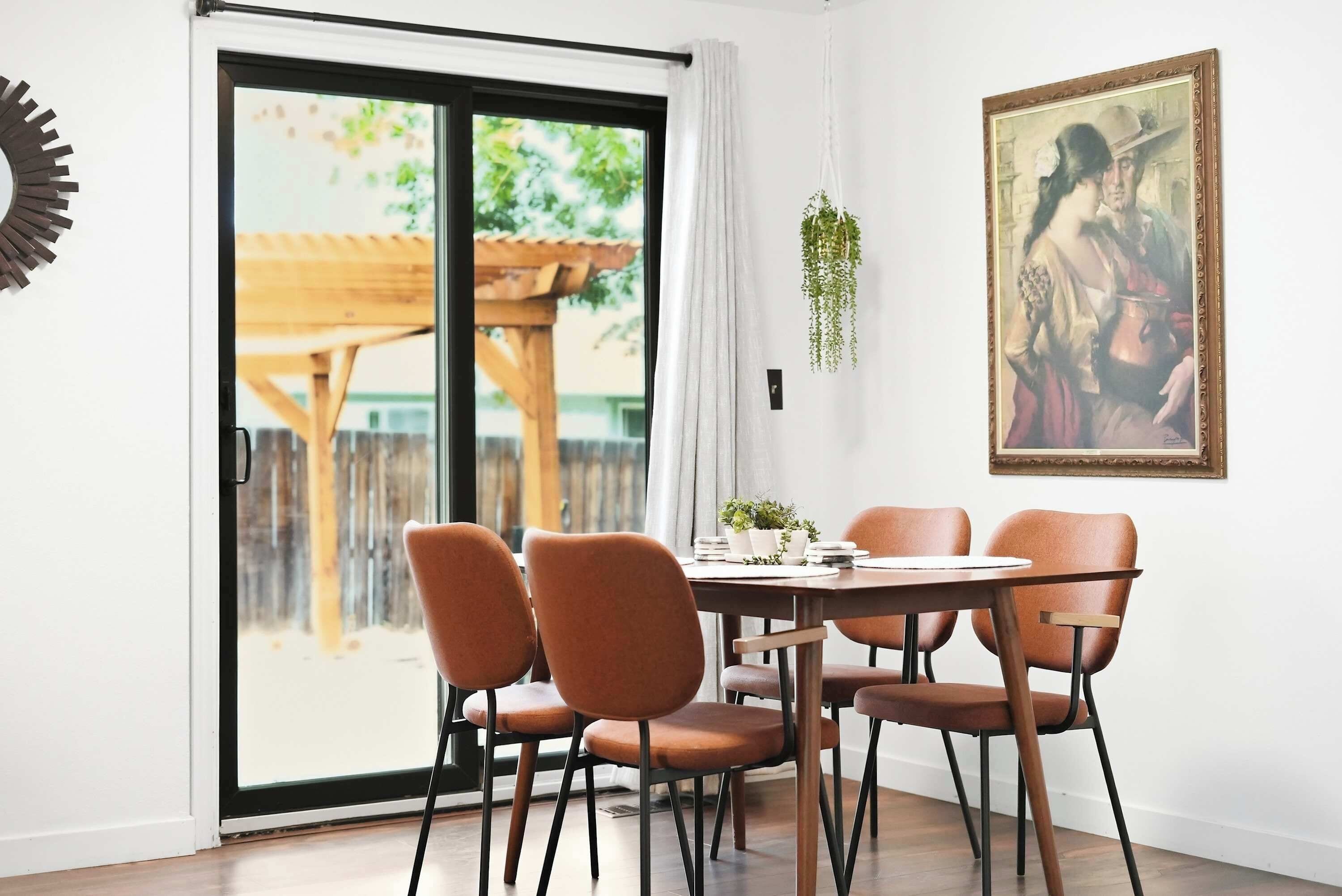 A dining area with a table and chairs, a sliding glass door leading to an outdoor space, and a framed painting on the wall.