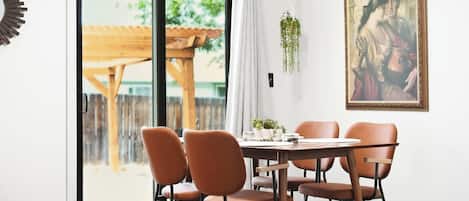A dining area with a table and chairs, a sliding glass door leading to an outdoor space, and a framed painting on the wall.