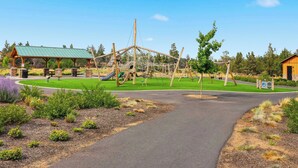 Ein Spielplatz mit einer Kletterkonstruktion, einem überdachten Sitzbereich und einem Gebäude mit Gründach.