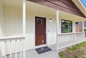 Une maison à l’extérieur blanc, avec une porte d’entrée marron et un porche doté d’une balustrade blanche.