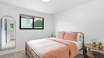 A bedroom with a bed, a bedside table, a mirror, and a window.