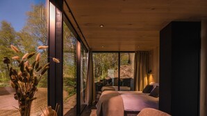 Ein modernes Schlafzimmer mit einem großen Bett, einer Sitzecke mit Tisch und Blick ins Freie.