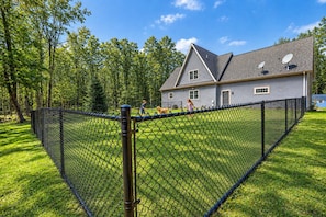 A fenced yard with a house in the background. - Forest Moon - Peaceful Pet-Friendly Wooded Retreat (Egg Harbor)