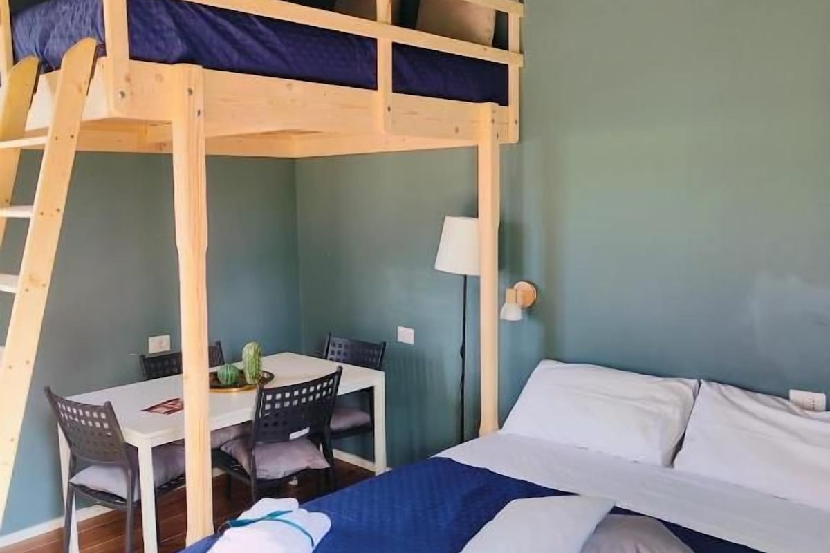 Un lit superposé avec un bureau et des chaises, un lit avec des oreillers et une lampe.