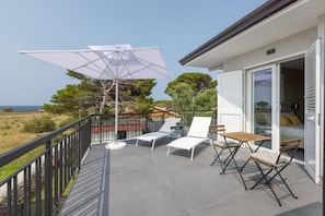 Un balcon avec vue sur la mer, aménagé avec des fauteuils de jardin blancs, une table et un parasol.