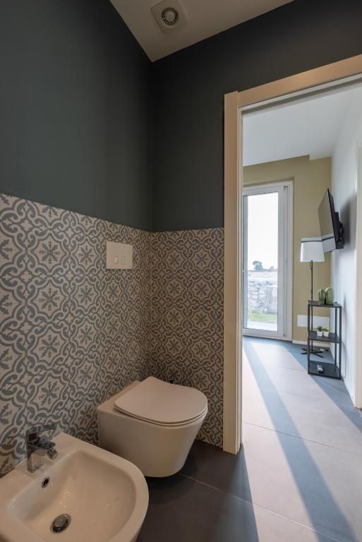 A bathroom with a toilet, sink, patterned wallpaper, and a view through an open door.