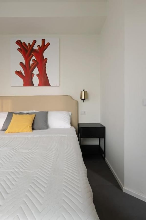 A bedroom with a bed, a nightstand, a wall-mounted lamp, and a painting.