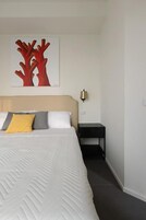 Un dormitorio con una cama, una mesita de noche, una lámpara de pared y un cuadro.