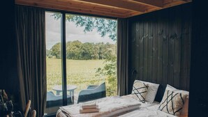 Ein Schlafzimmer mit großem Fenster, einem Bett mit Kissen, einem Tisch und einem Stuhl.