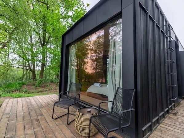 Een moderne buitenruimte met een bed, twee stoelen en een bijzettafeltje.