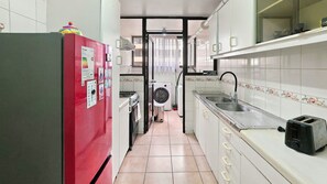 A narrow kitchen with a red refrigerator, a washing machine, and a sink with a faucet.