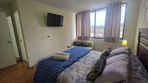 Habitació d'hotel amb llit, televisió penjada a la paret, finestra amb cortines i vista exterior.