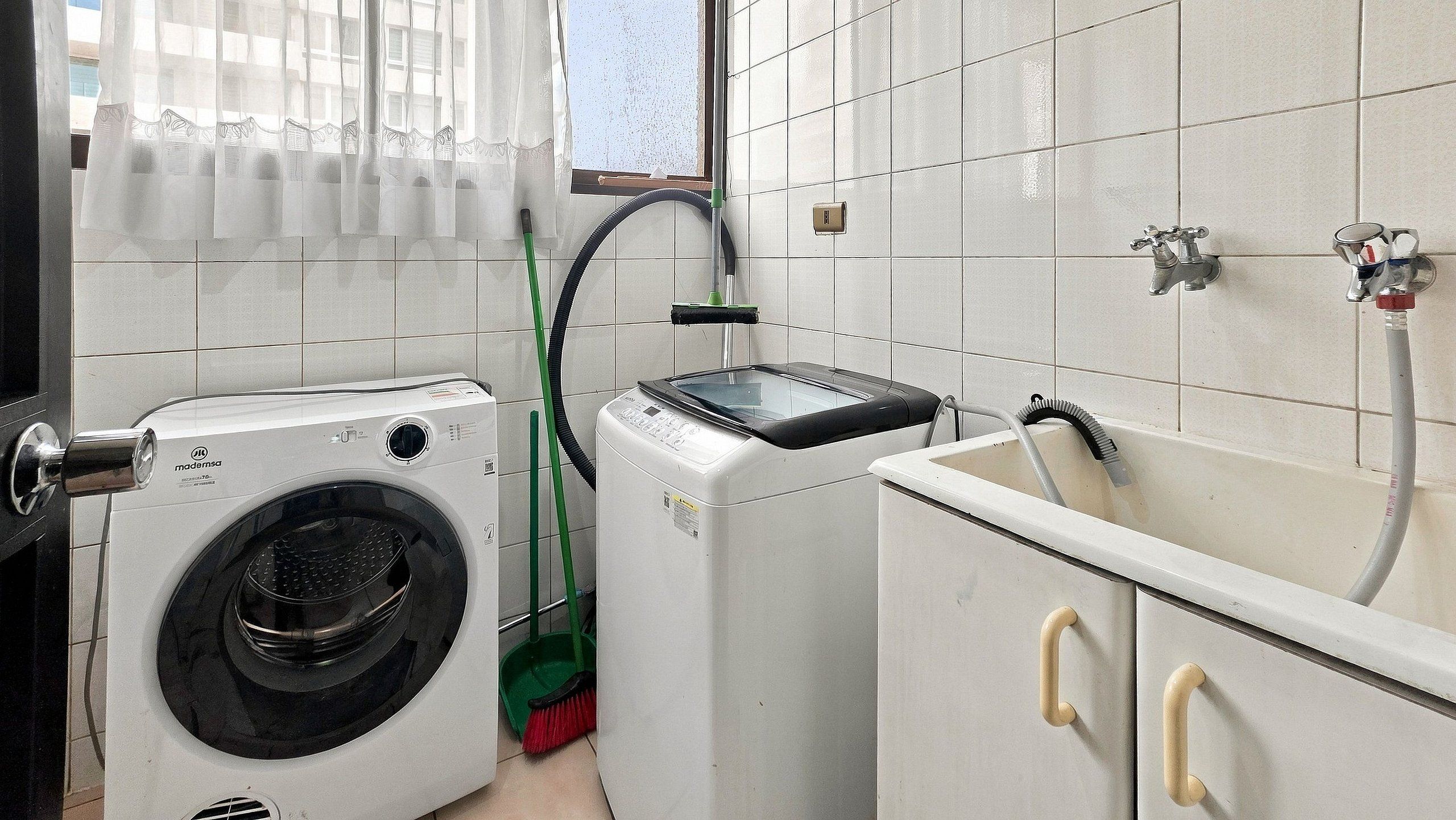 Ein Waschraum mit einer Waschmaschine und einem Trockner, einem Mop, einer Bürste und einem Schlauch.