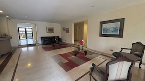 Eine geräumige Lobby mit einer Rezeption, einem schwarzen Ledersofa, einem Glastisch und einem gerahmten Gemälde an der Wand.