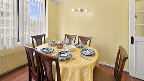 A dining room with a table set for four, chairs, and a window with sheer curtains.