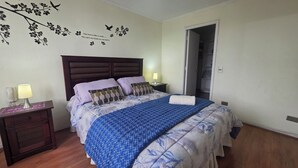 Ein Schlafzimmer mit einem Bett, einem Nachttisch, einer Lampe, einer Wanddekoration und einer Tür zu einem Kleiderschrank.