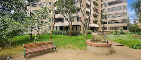 Um parque com um banco, árvores e um edifício com varandas múltiplas.
