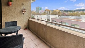 A balcony with a table and chairs, a textured wall, and a view of buildings in the distance.