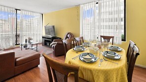 A dining area with a table set for four, a sofa, and a television in the background.