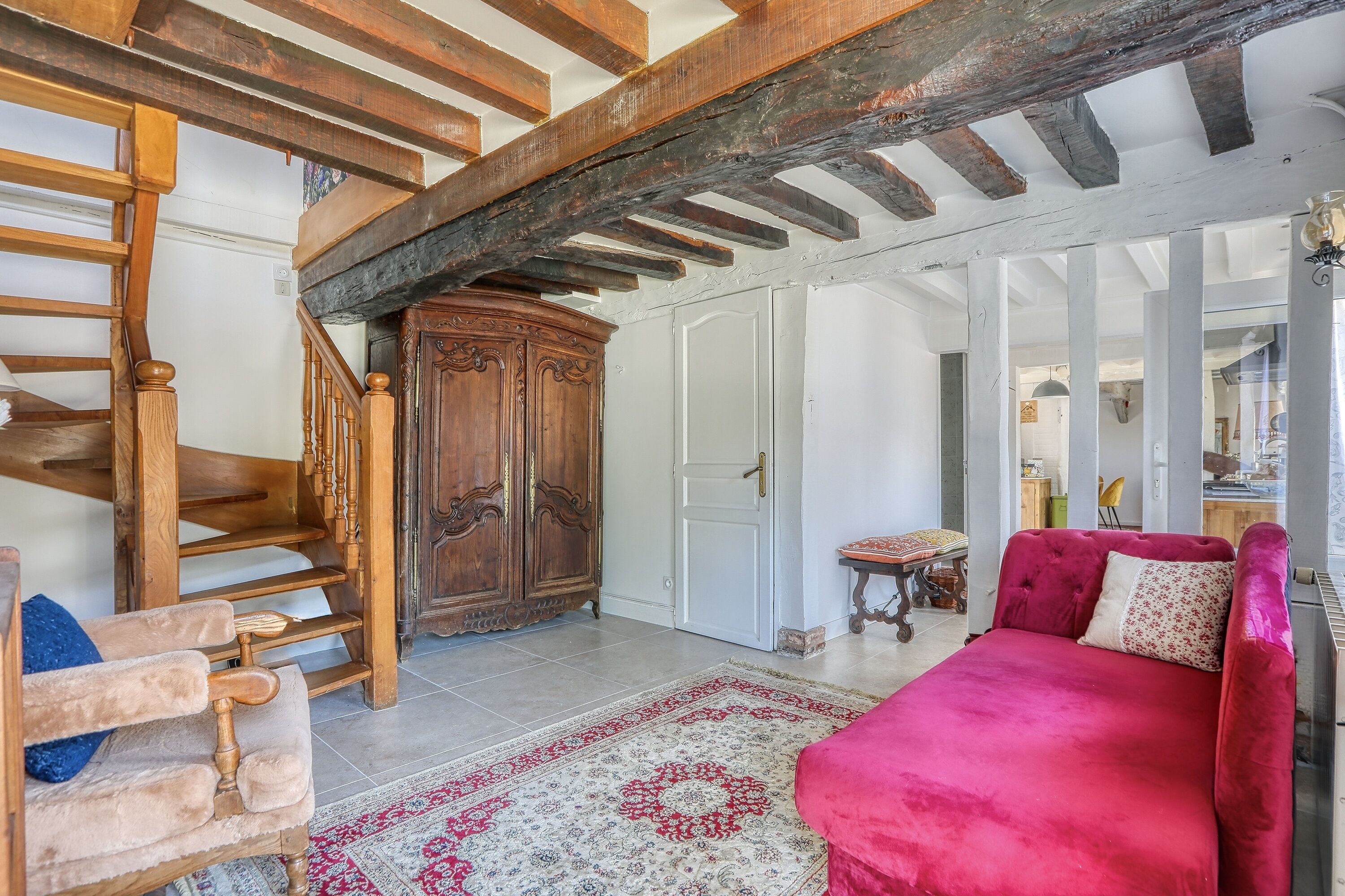 Ein Zimmer mit einer Holztreppe, einem roten Sofa, einem gemusterten Teppich und einem traditionellen Holzschrank.