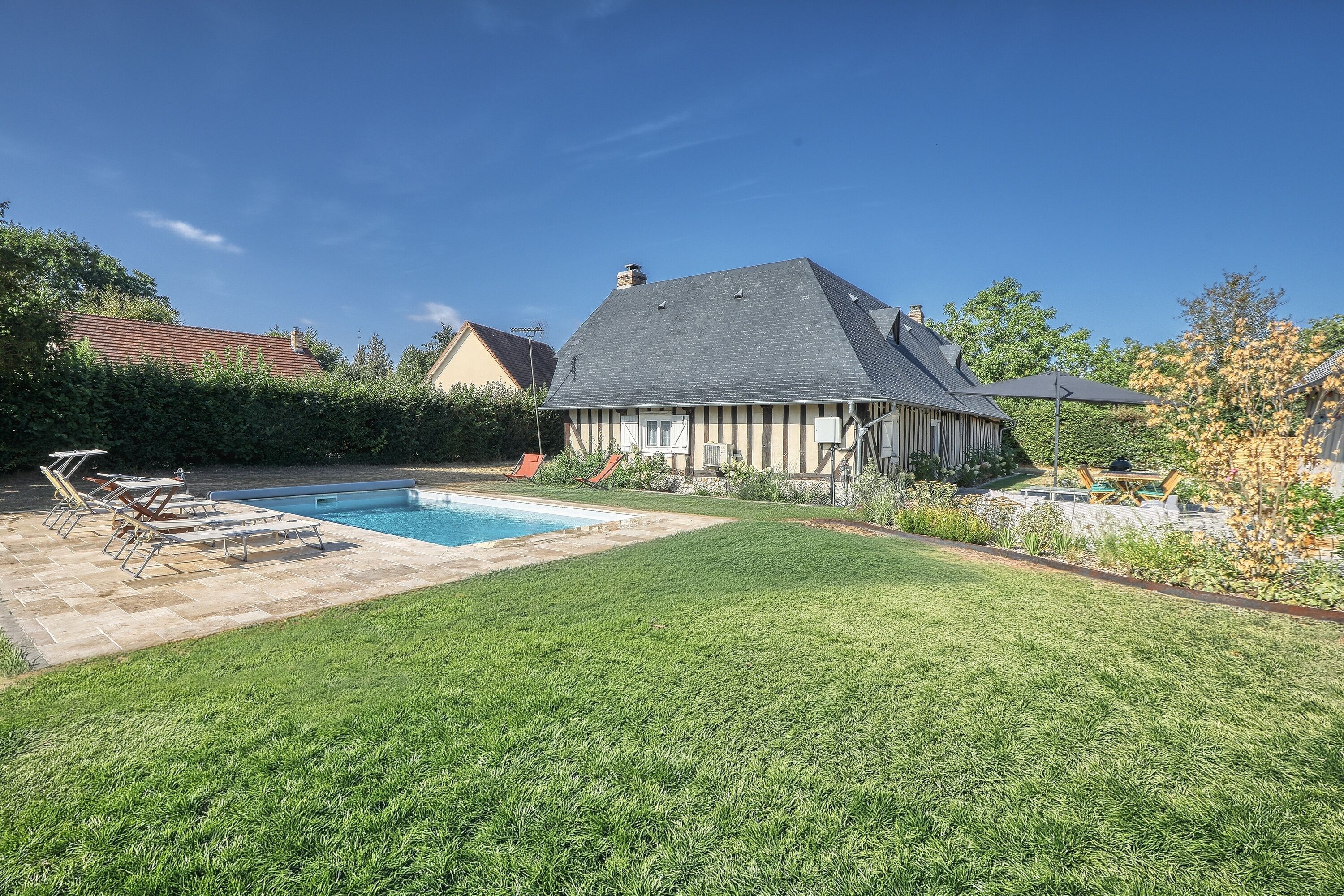 Ein Haus mit Swimmingpool, einem gepflegten Rasen und einem Garten.