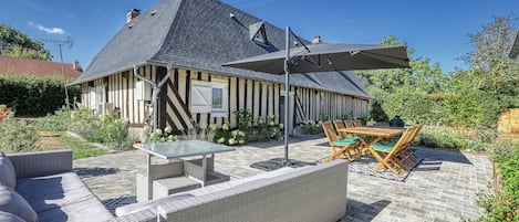 A traditional half-timbered house with a sloped roof, a patio with outdoor furniture, and a garden area.