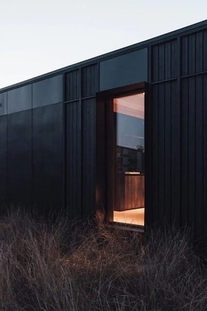 Un bâtiment moderne, à l’extérieur sombre, avec une seule porte ouverte donnant accès à un espace intérieur.