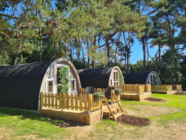 Twee kleine, gedeeltelijk open hutten met houten omheiningen en een gazon ervoor.