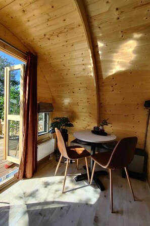Een houten interieur met een ronde tafel en stoelen, een raam met gordijnen en een radiator.