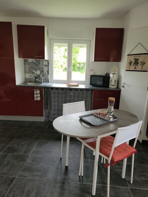 A compact kitchen with a dining area, featuring a microwave, coffee maker, and a window with a view of greenery. - Vrbo Property (Pommeuse)