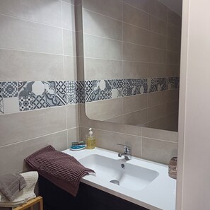 A bathroom with a white sink, a mirror, and patterned tiles on the wall. - Vrbo Property (Pommeuse)