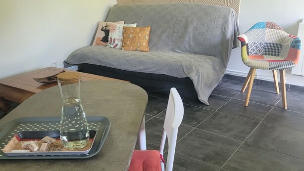 A dining area with a table, chairs, and a sofa in the background.