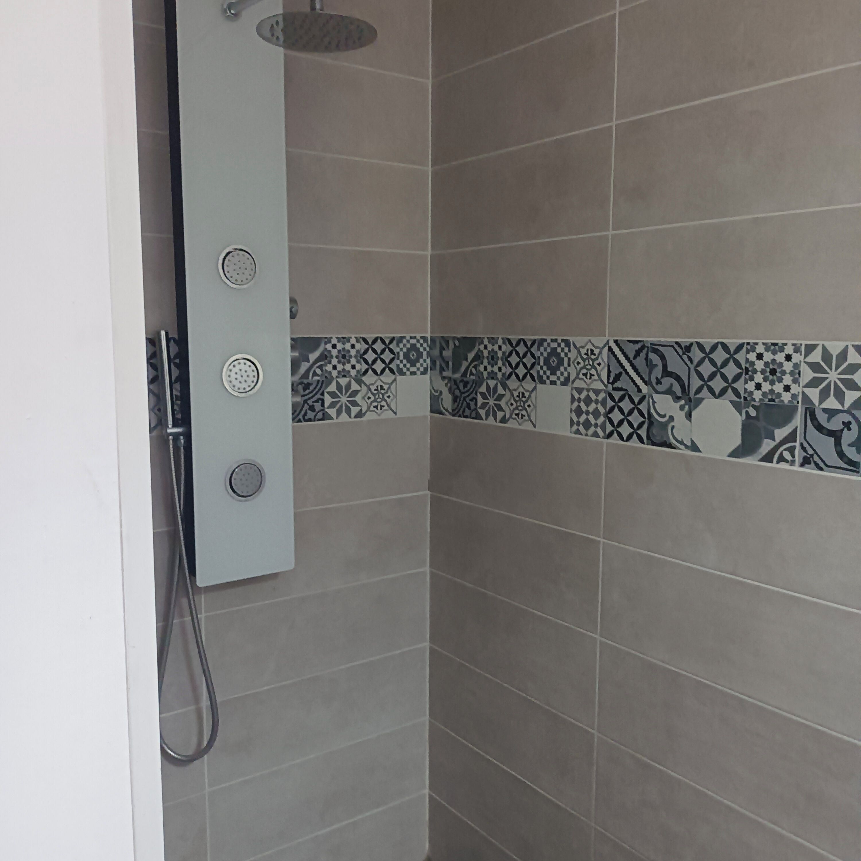 Een douchecabine met een handdouche en een bedieningspaneel aan de muur.